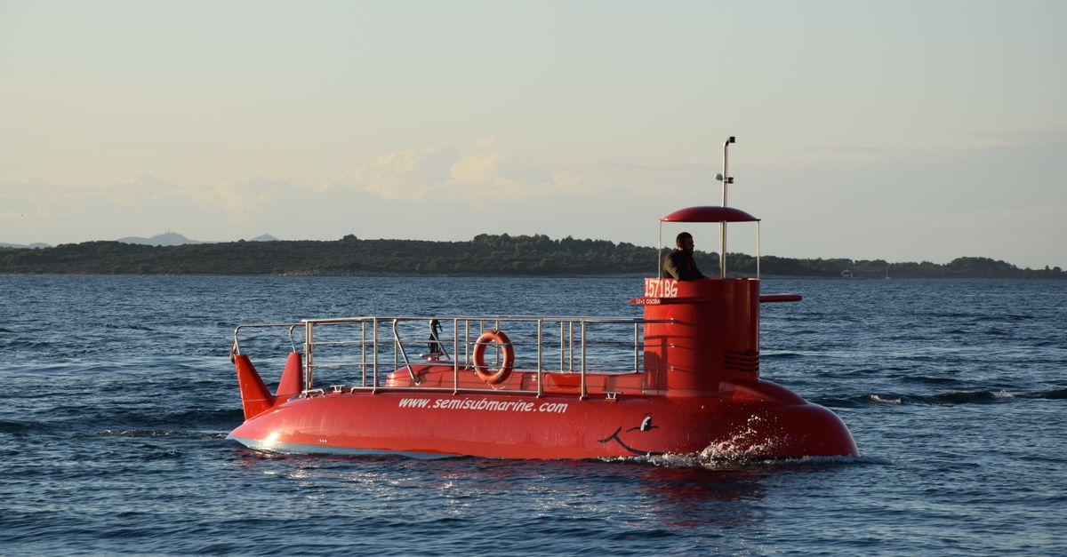 A bright red semi-submarine cruising on a calm ocean with a distant shoreline.